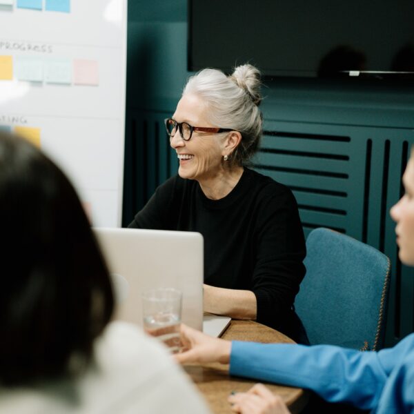 Woman in black sweater and eyeglasses sitting on chair beside woman in blue shirt in a meeting